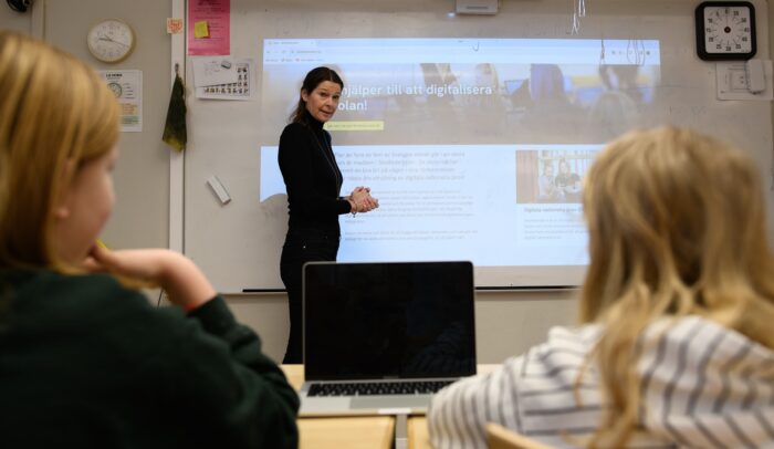 En kvinna står framför ett klassrum.