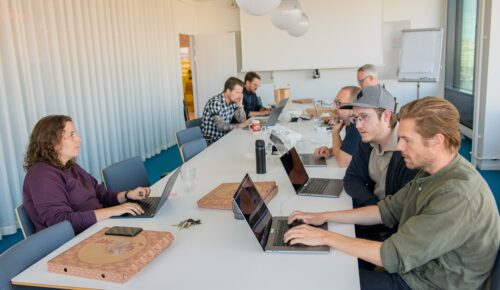 En grupp människor som sitter runt ett bord med bärbara datorer.