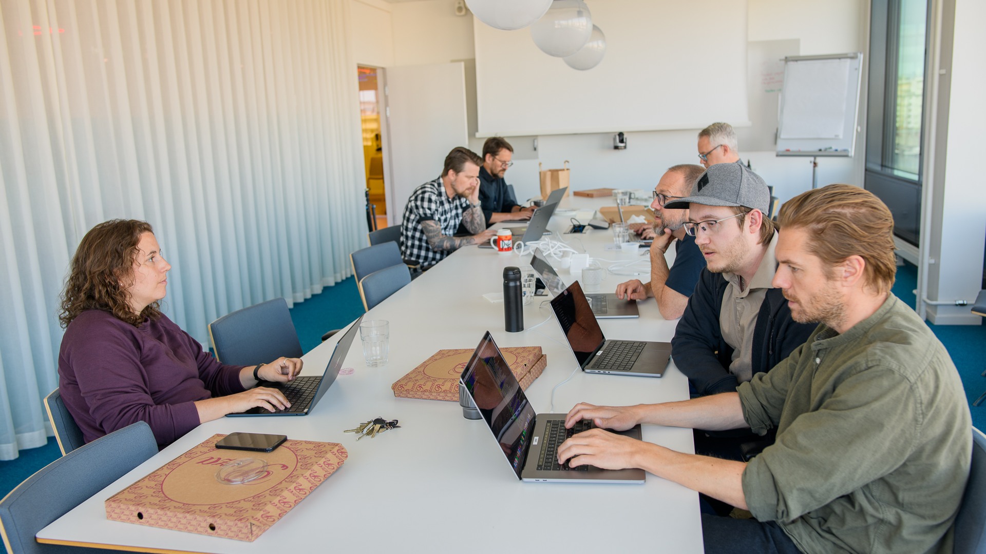 En grupp människor som sitter runt ett bord med bärbara datorer.