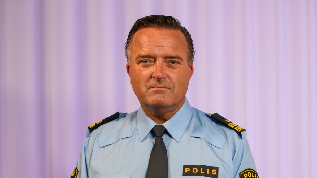 Jan Olsson i polisuniform står framför en ridå.