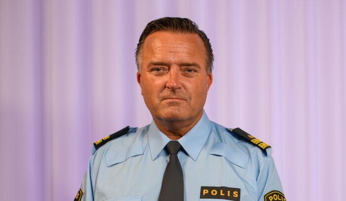 Jan Olsson i polisuniform står framför en ridå.