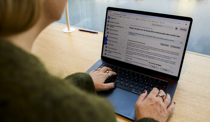 En kvinna sitter framför en dator och kollar upp hur man gör en minnessida på facebook.