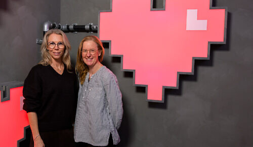 Två kvinnor står framför en stor skylt som föreställer ett rött hjärta.