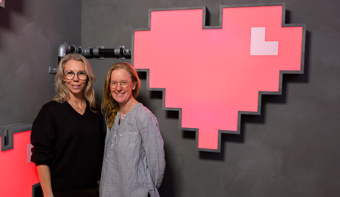 Två kvinnor står framför en stor skylt som föreställer ett rött hjärta.