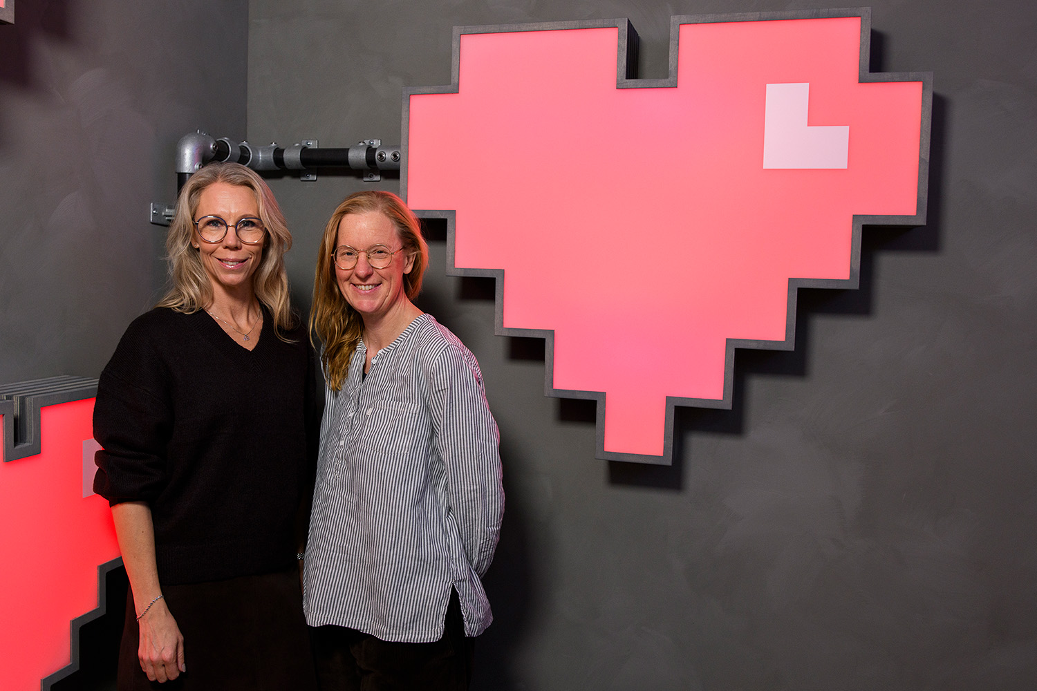 Två kvinnor står framför en stor skylt som föreställer ett rött hjärta.