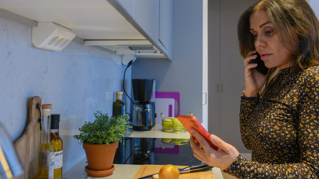 Kvinna som tjuvkollar sin partners mobiltelefon medan hon lagar mat.