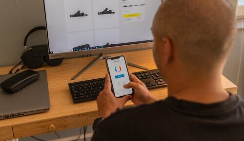 Man sitter framför datorn, har en nätbutik i webbläsaren. Håller mobil i handen med Swish-appen öppen.
