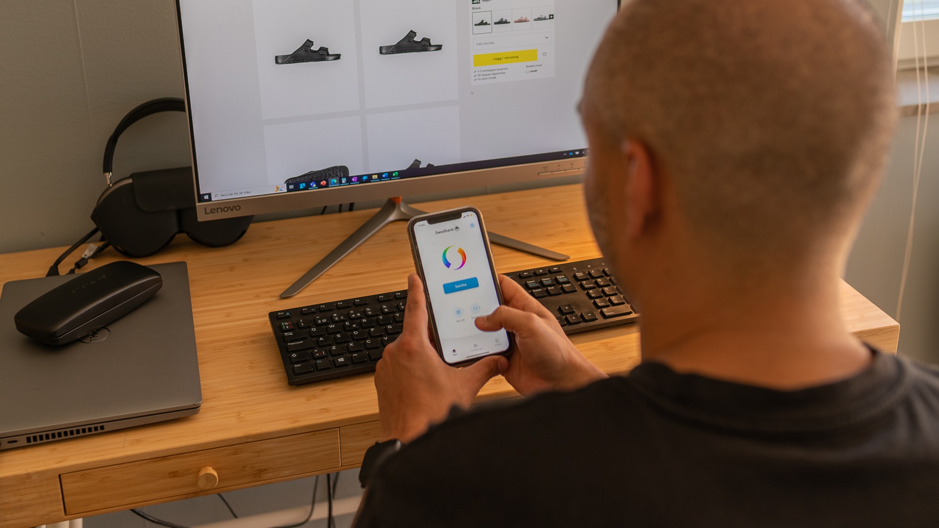 Man sitter framför datorn, har en nätbutik i webbläsaren. Håller mobil i handen med Swish-appen öppen.