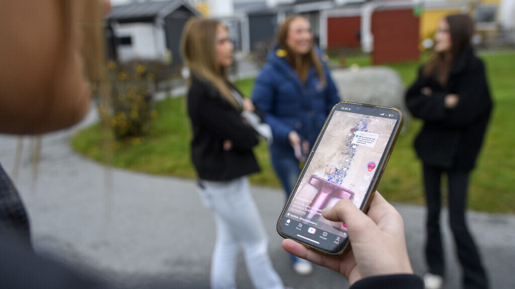 En grupp ungdomar står ute och använder en mobiltelefon. Åldersgränser på sociala medier.