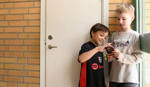 Två barn tittar tillsammans på en mobiltelefon.