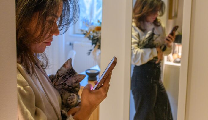 En kvinna tittar på sin telefon medan hon håller i en katt.