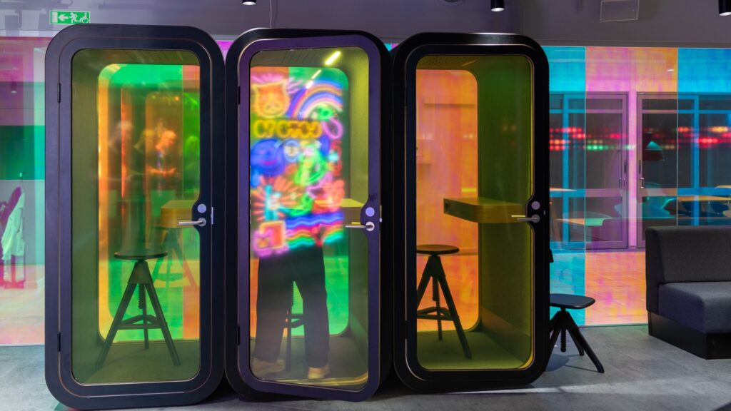 Tre telefonbås, i glasdörren syns en reflektion av neonskyltar.