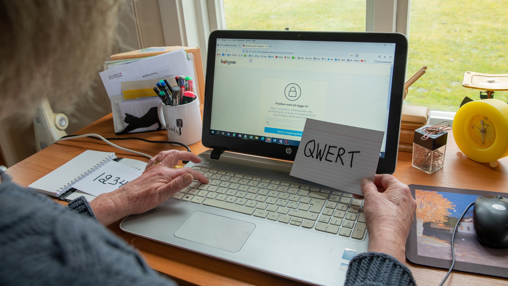 Person framför datorskärm håller i en lapp med ett lösenord skrivet.