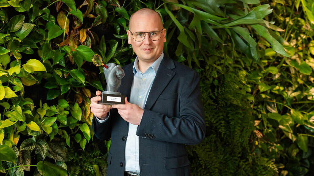 Ett porträtt av it-säkerhetsspecialisten Karl Emil Nikka framför en växtvägg med priset Det gyllene förstoringsglaset i handen.