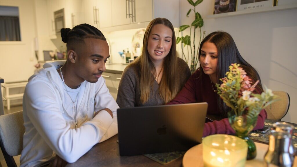 Tre ungdomar sitter framför en datorskärm och tittar på något.