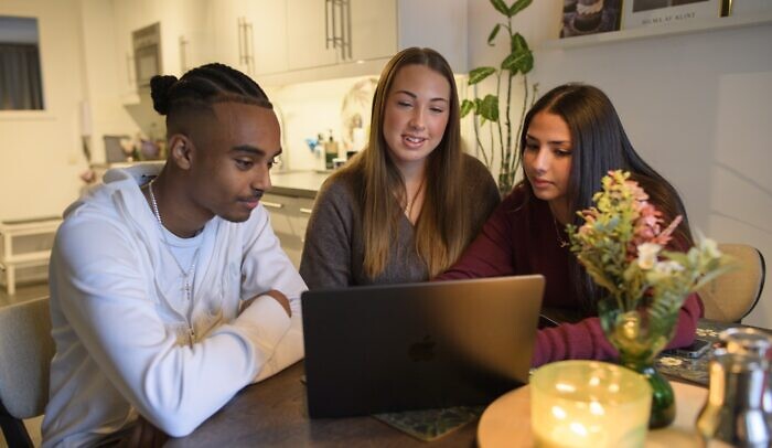 Tre ungdomar sitter framför en datorskärm och tittar på något.
