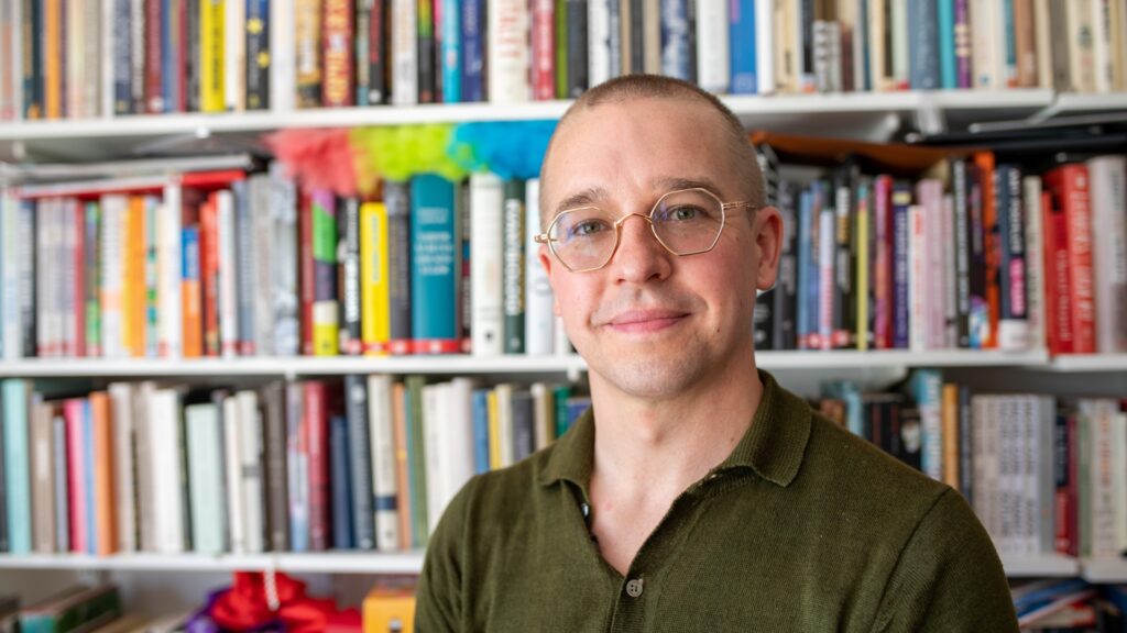Niklas Laninge står framför en bokhylla med färgglada böcker.