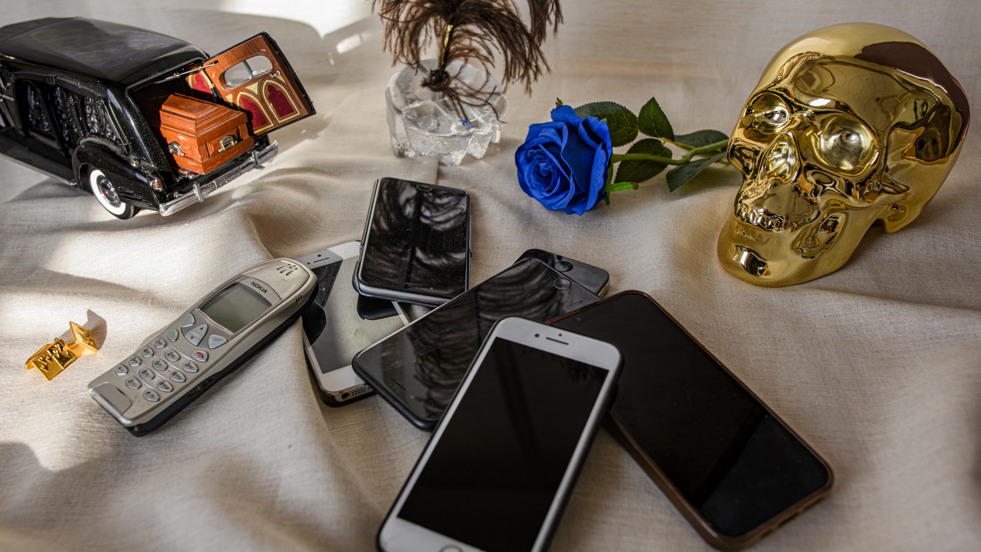 Många mobiltelefoner av olika ålder ligger på ett bord bredvid en leksaksbil med en likkista i.