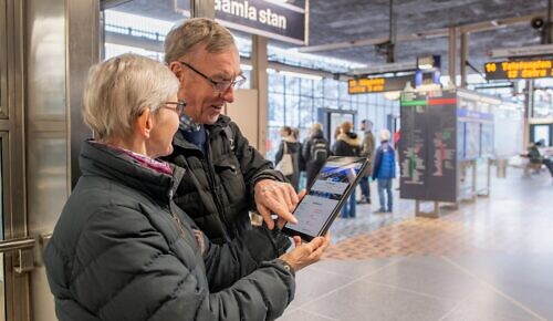 Äldre par står i tunnelbanan och använder en surfplatta.