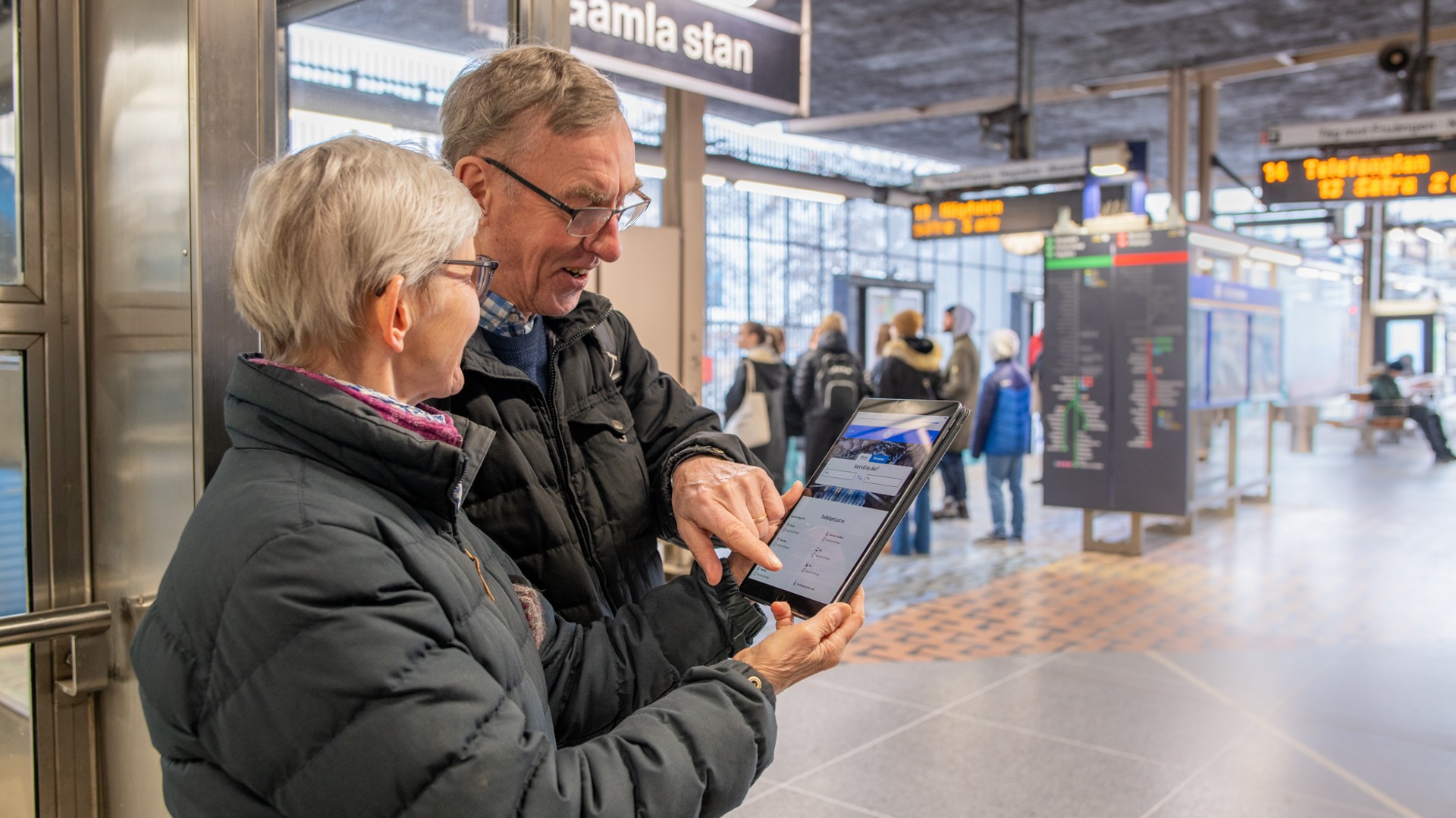 Äldre par står i tunnelbanan och använder en surfplatta.